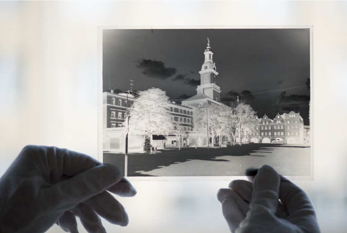 Trzymany w dłoniach negatyw szklany przedstawiający budynek. Fotografia czarno-biała.